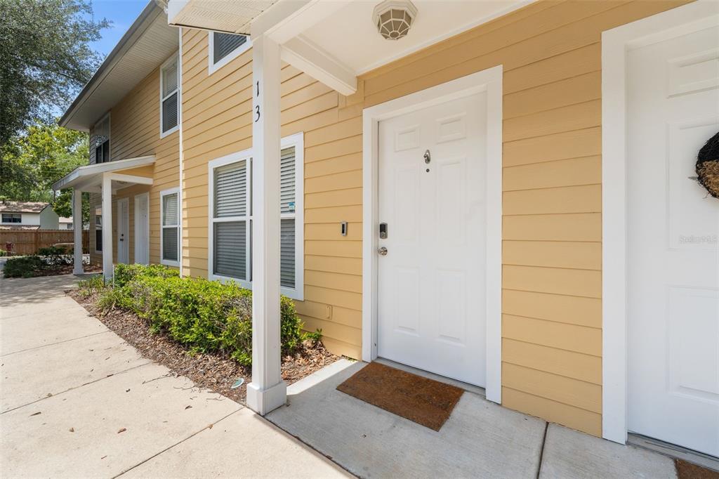 A tan, two-story apartment building exterior features a white front door and a concrete walkway — 2636 SW 35TH PLACE UNIT 13, GAINESVILLE, FL
