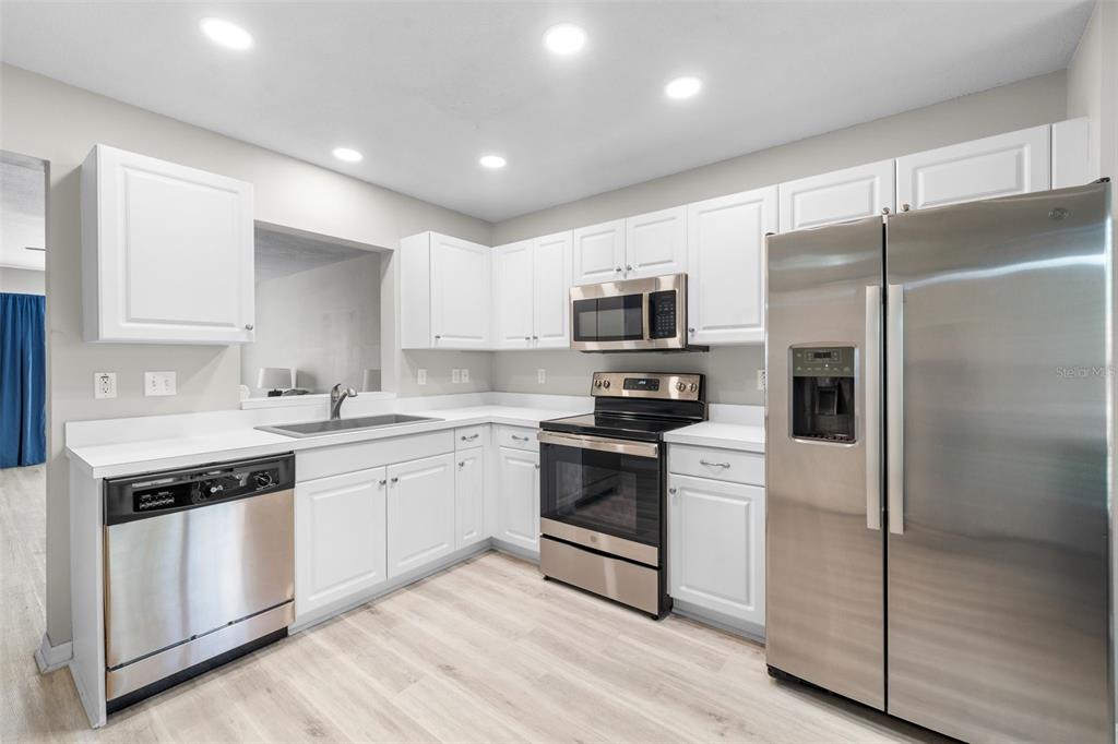 A kitchen with white cabinets, stainless steel appliances, and light-colored wood-look flooring — 2636 SW 35TH PLACE UNIT 13, GAINESVILLE, FL
