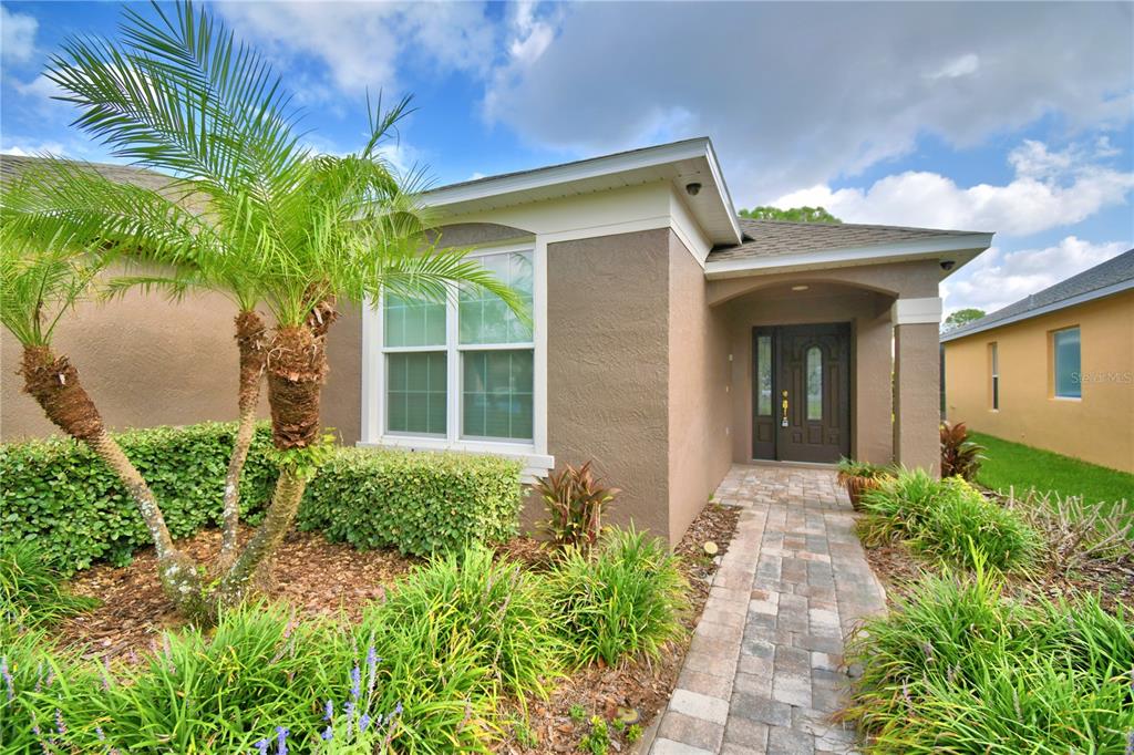 A tan stucco house features a palm tree, a paved walkway, and a dark front door — 3034 BARBADOS LANE, HAINES CITY, FL