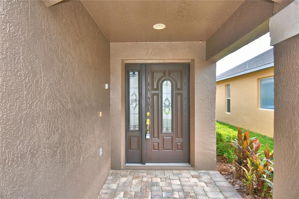 A covered entryway features a brown front door with glass inserts and paver flooring — 3034 BARBADOS LANE, HAINES CITY, FL