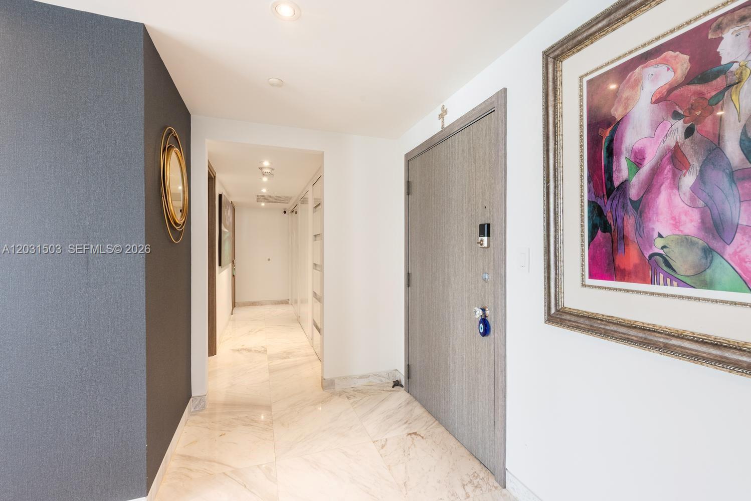 A hallway with marble floors leads to a doorway with a framed painting nearby — 5660 Collins Ave # 14C, Miami Beach FL 33140, MIAMI BEACH, FL