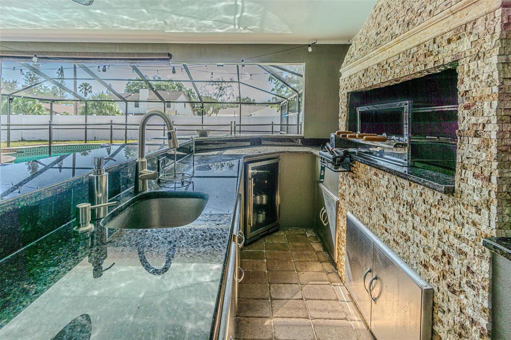 An outdoor kitchen features a granite countertop, a sink, a beverage cooler, and a grill — 6728 RANGER DRIVE, TAMPA, FL