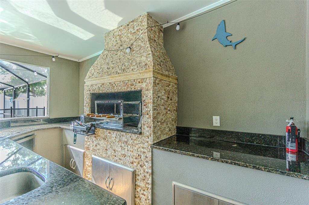 An outdoor kitchen features a stone-clad grill, dark granite countertops, and a stainless steel fire extinguisher — 6728 RANGER DRIVE, TAMPA, FL