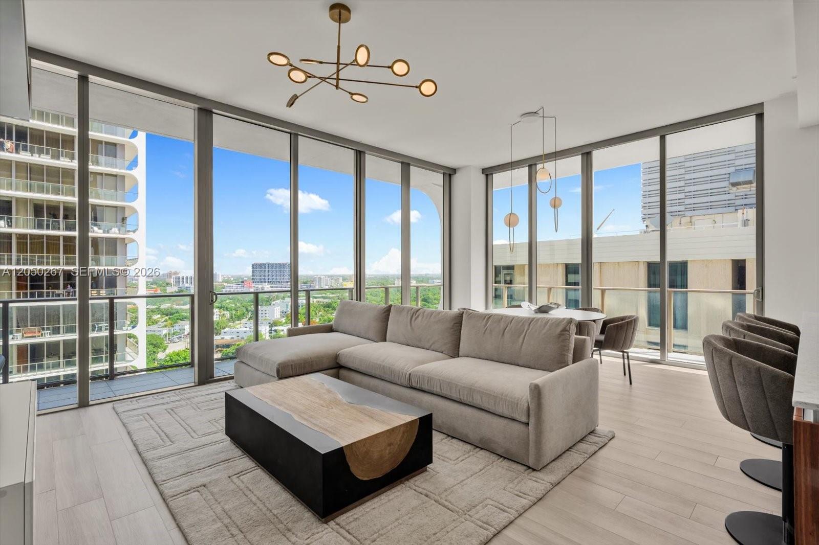 A modern living room features a grey sectional sofa, wood-accented coffee table, and floor-to-ceiling windows — 2655 S Bayshore Dr # 1412, Miami FL 33133, MIAMI, FL