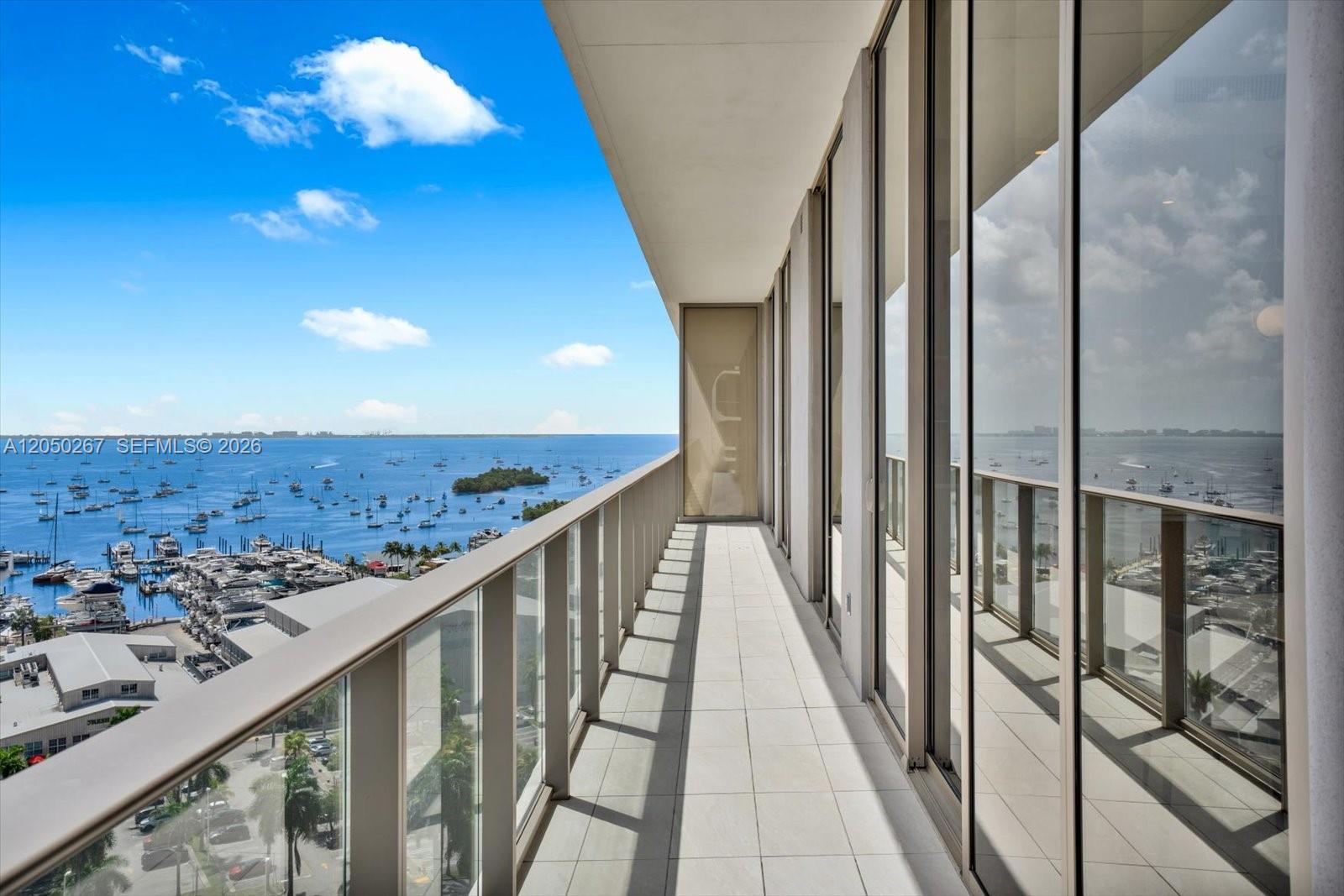 A high-rise balcony features glass railings, light-colored tile flooring, and a view of a marina — 2655 S Bayshore Dr # 1412, Miami FL 33133, MIAMI, FL