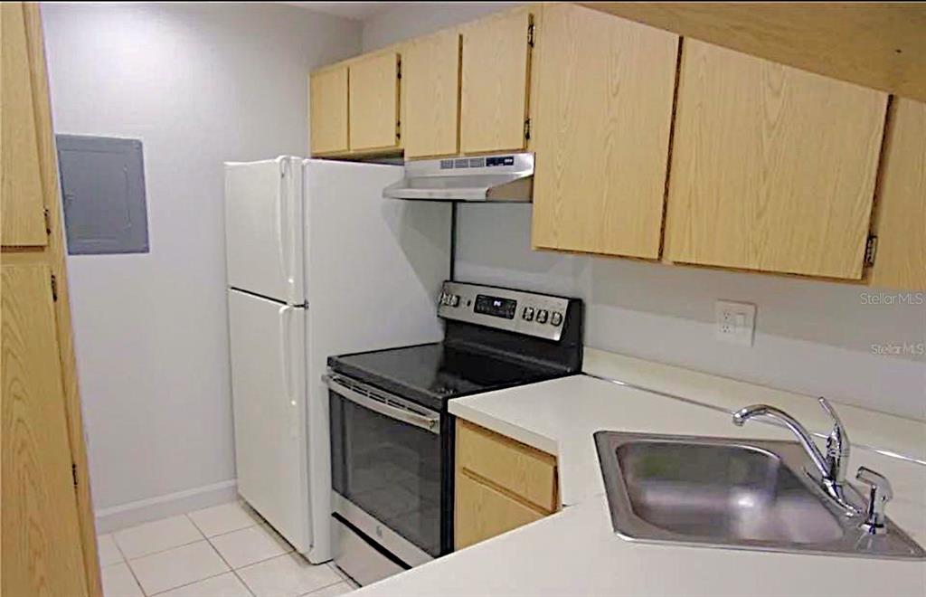 A kitchen features light wood cabinets, white appliances, a stainless steel sink, and tile flooring — 1344 PINE RIDGE CIRCLE E UNIT E3, TARPON SPRINGS, FL