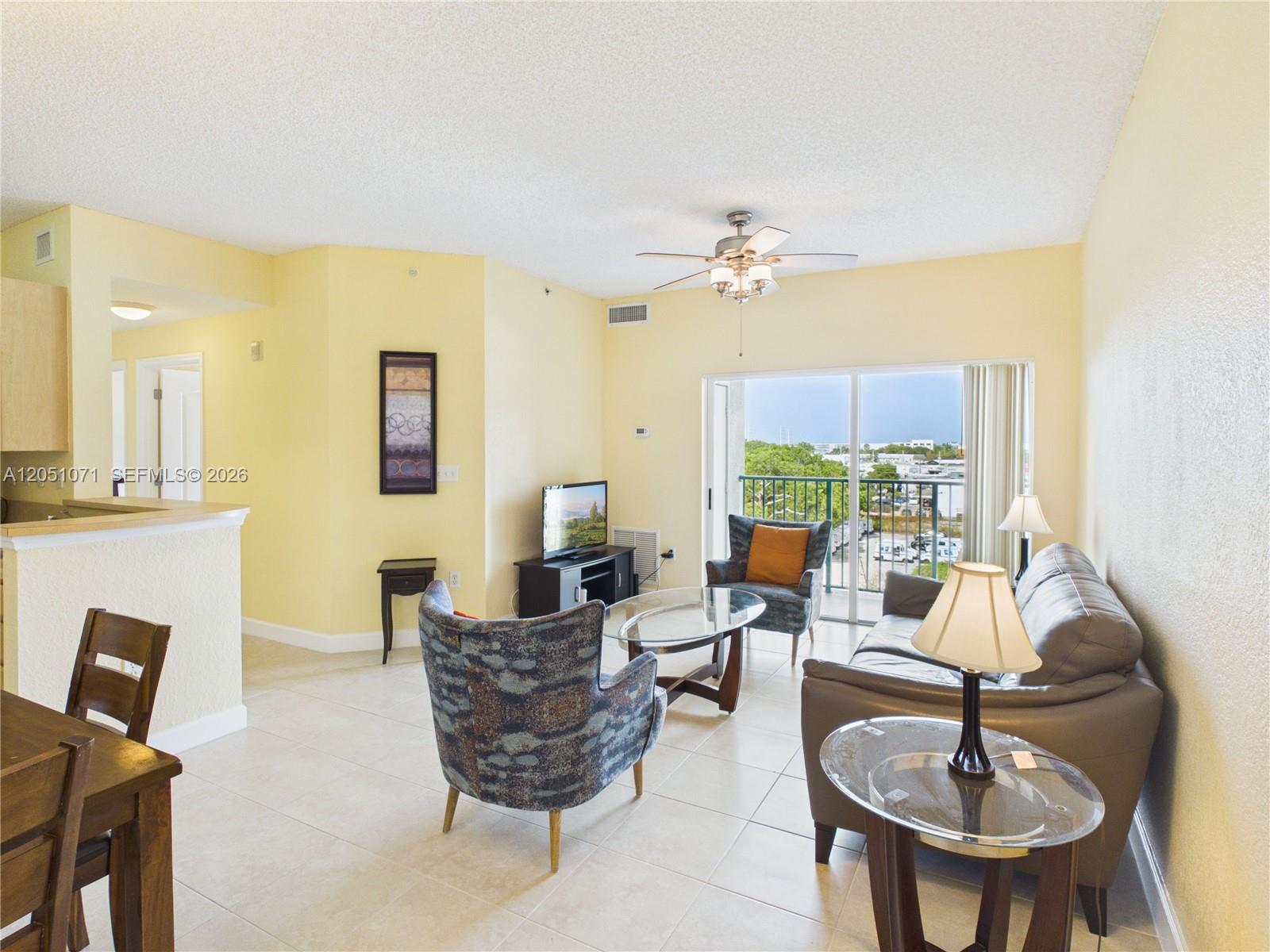 A living room with yellow walls, tile flooring, a ceiling fan, and a balcony view — 6001 SW 70th St # 502, South Miami FL 33143, SOUTH MIAMI, FL