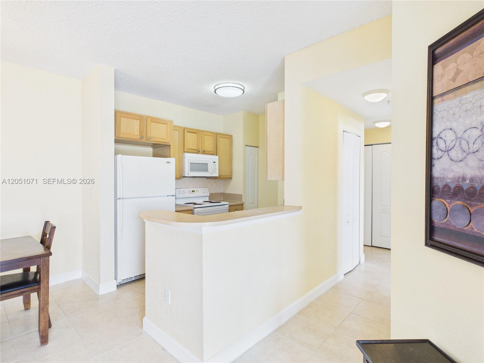 A kitchen features light wood cabinets, white appliances, and a breakfast bar — 6001 SW 70th St # 502, South Miami FL 33143, SOUTH MIAMI, FL