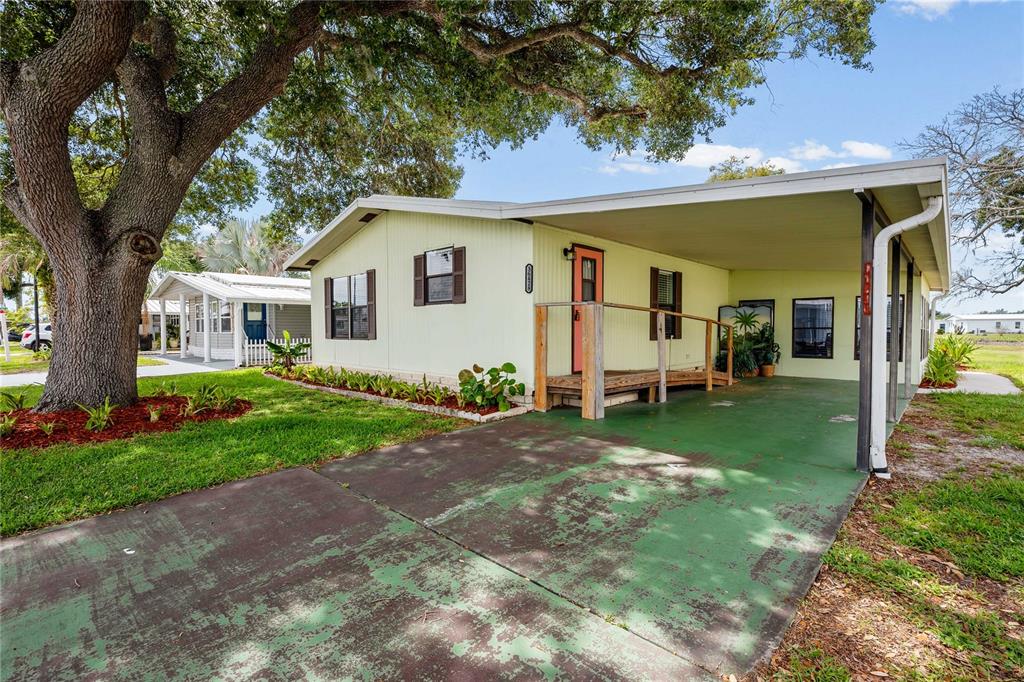 A pale yellow mobile home features a green painted driveway and a wooden wheelchair ramp — 36428 MALIBU WAY, ZEPHYRHILLS, FL