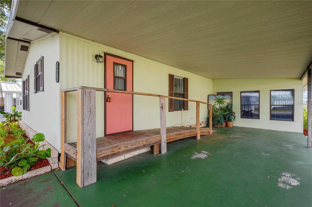 A mobile home exterior features a salmon-colored door, a wooden ramp, and a green carport — 36428 MALIBU WAY, ZEPHYRHILLS, FL