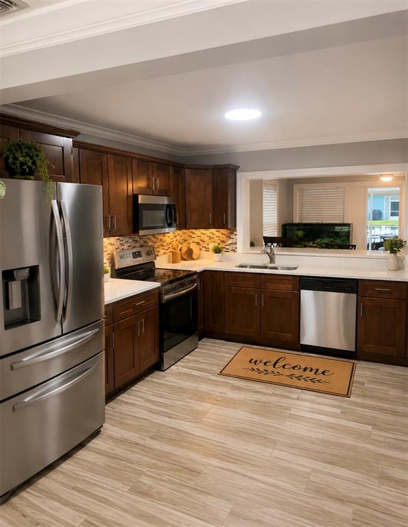 A kitchen features dark wood cabinets, stainless steel appliances, white countertops, and light wood flooring — 1623 WAVECREST STREET, MERRITT ISLAND, FL