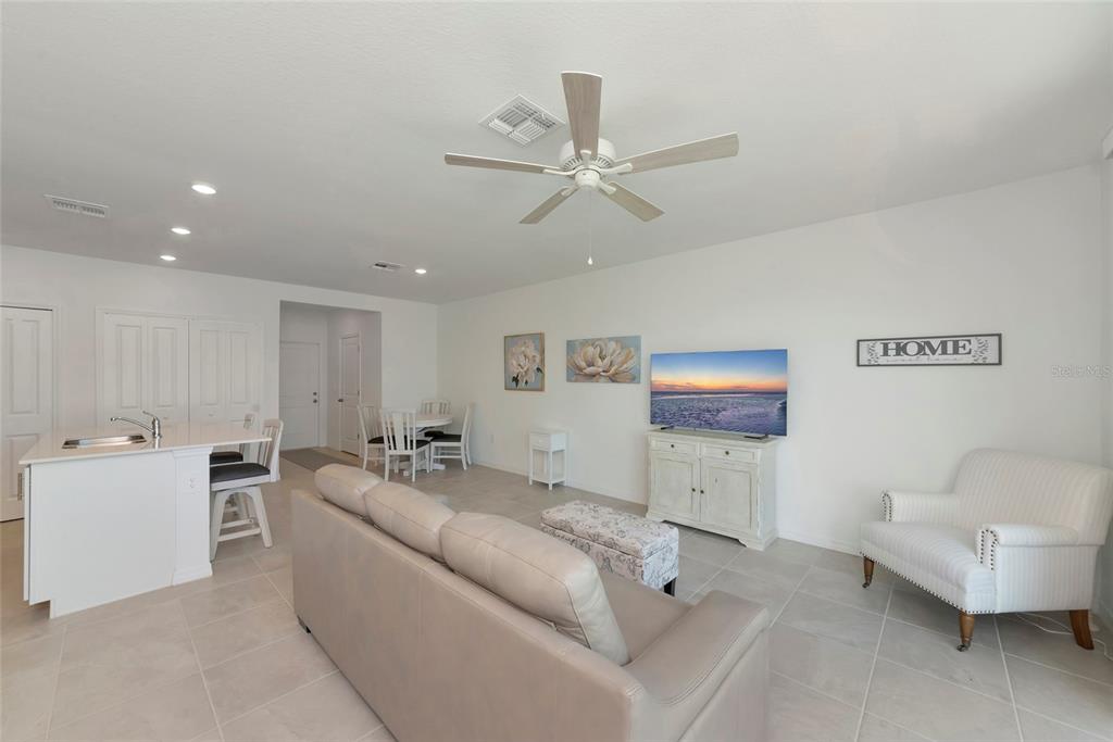 An open-concept living and dining area features a kitchen island, neutral tile floors, and furniture — 14251 LILAC SKY TERRACE, BRADENTON, FL