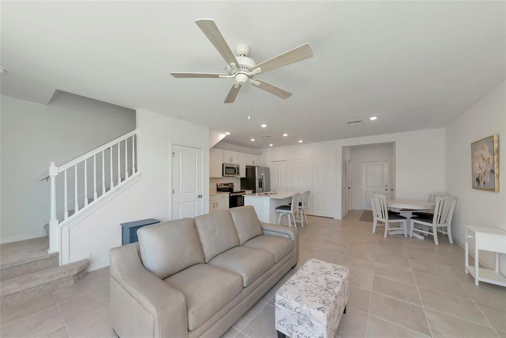An open-concept living room and kitchen featuring a light gray sofa, tile flooring, and stairs — 14251 LILAC SKY TERRACE, BRADENTON, FL