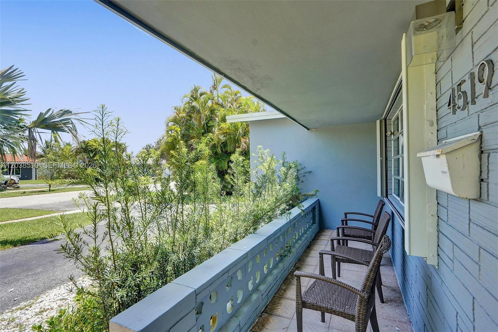 A covered porch features a decorative concrete railing, tiled flooring, and three wicker chairs — 4519 Monroe St, Hollywood FL 33021, HOLLYWOOD, FL