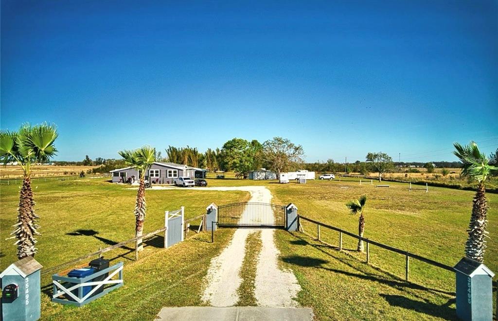 A gravel driveway leads through a gated entrance to a house on a large lot — 35495 SINGLETARY ROAD, MYAKKA CITY, FL