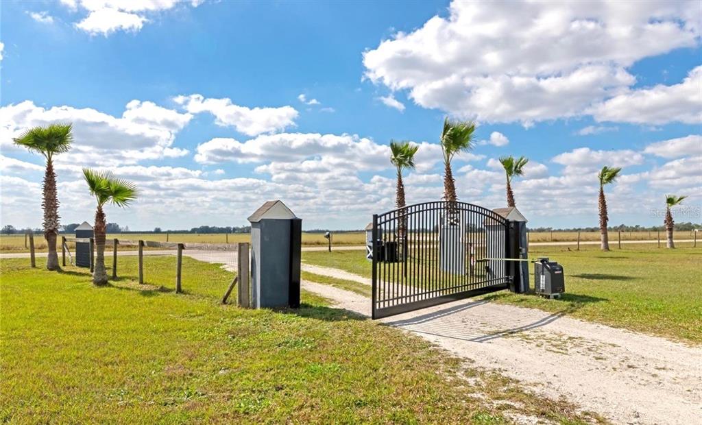 A black metal gate stands at the entrance of a grassy field with palm trees — 35495 SINGLETARY ROAD, MYAKKA CITY, FL