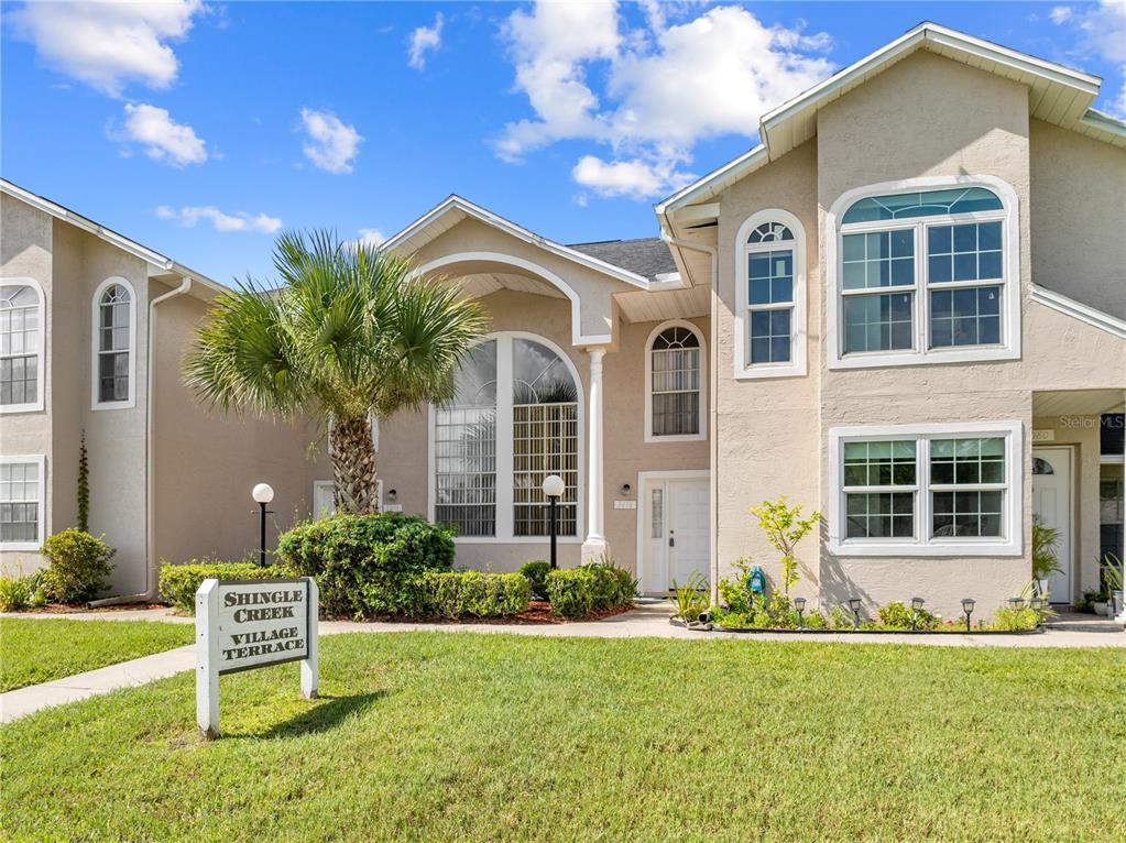 A two-story tan stucco townhouse with a palm tree and a community sign in front — 3078 SHINGLE CREEK COURT, KISSIMMEE, FL