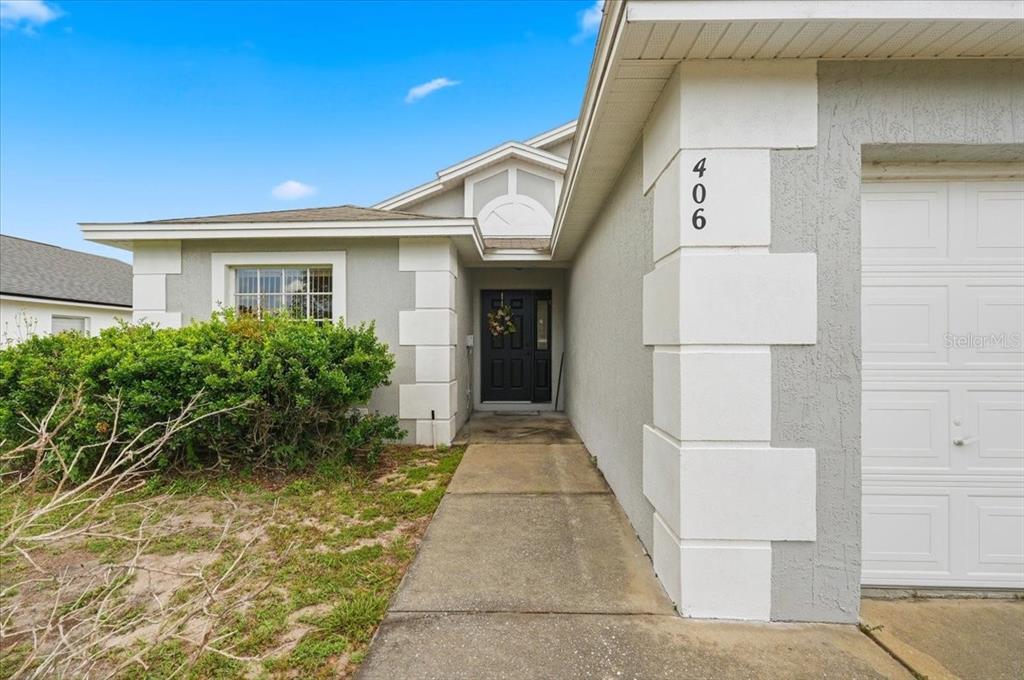 A gray house exterior features a concrete walkway leading to a dark front door — 406 SAINT ANNS DRIVE, WINTER HAVEN, FL