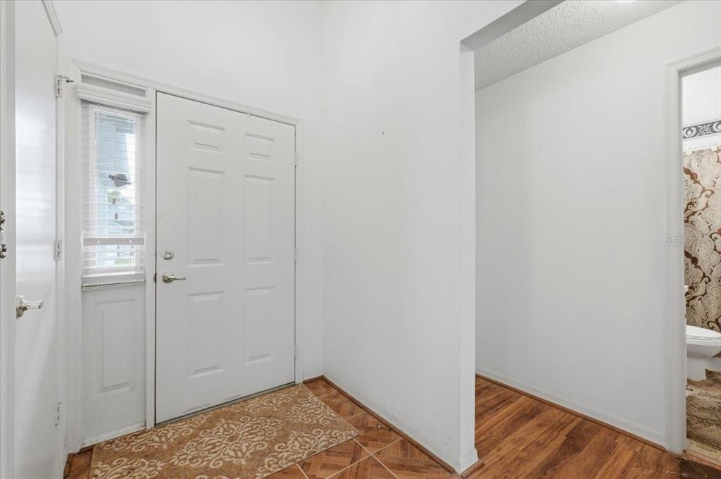 An entryway features a white front door, tiled flooring, and a doorway leading to a bathroom — 406 SAINT ANNS DRIVE, WINTER HAVEN, FL