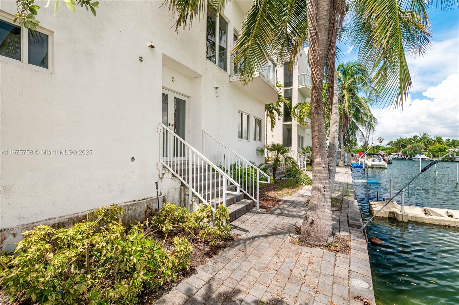A white building exterior features a staircase leading to a doorway beside a canal — 1975 Calais Dr, Miami Beach FL 33141, MIAMI BEACH, FL