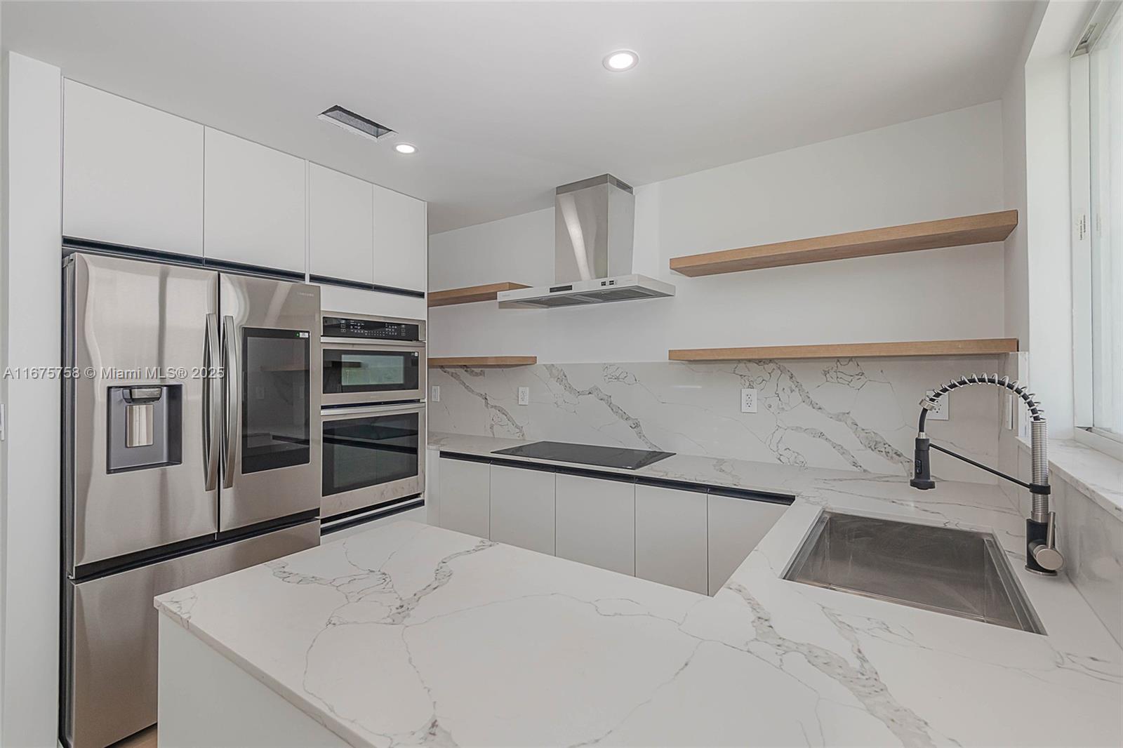 A modern kitchen features white cabinets, marble countertops, stainless steel appliances, and floating wood shelves — 1975 Calais Dr, Miami Beach FL 33141, MIAMI BEACH, FL