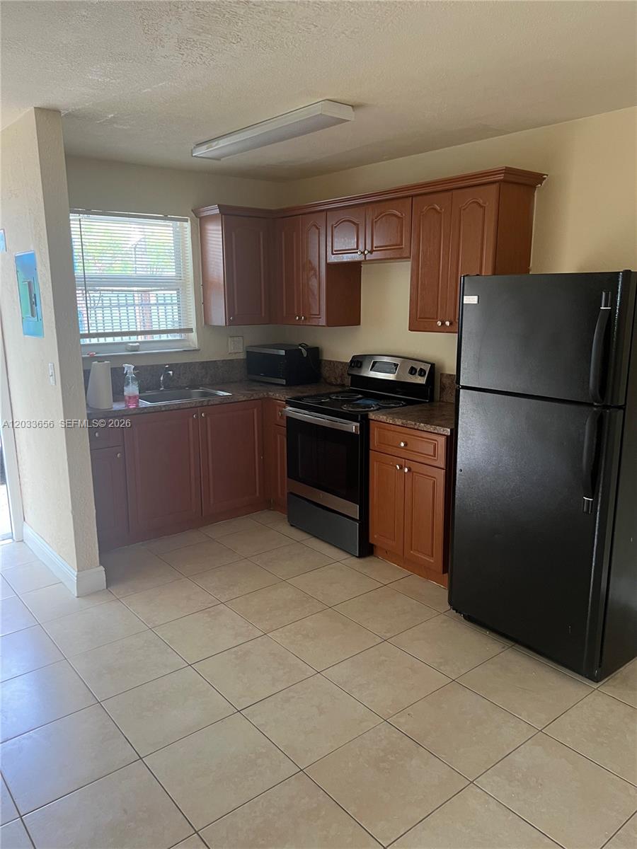 A kitchen features wood cabinets, a black refrigerator, a stove, and light-colored floor tiles — 5900 NW 1st Ave # 2, Miami FL 33127, MIAMI, FL