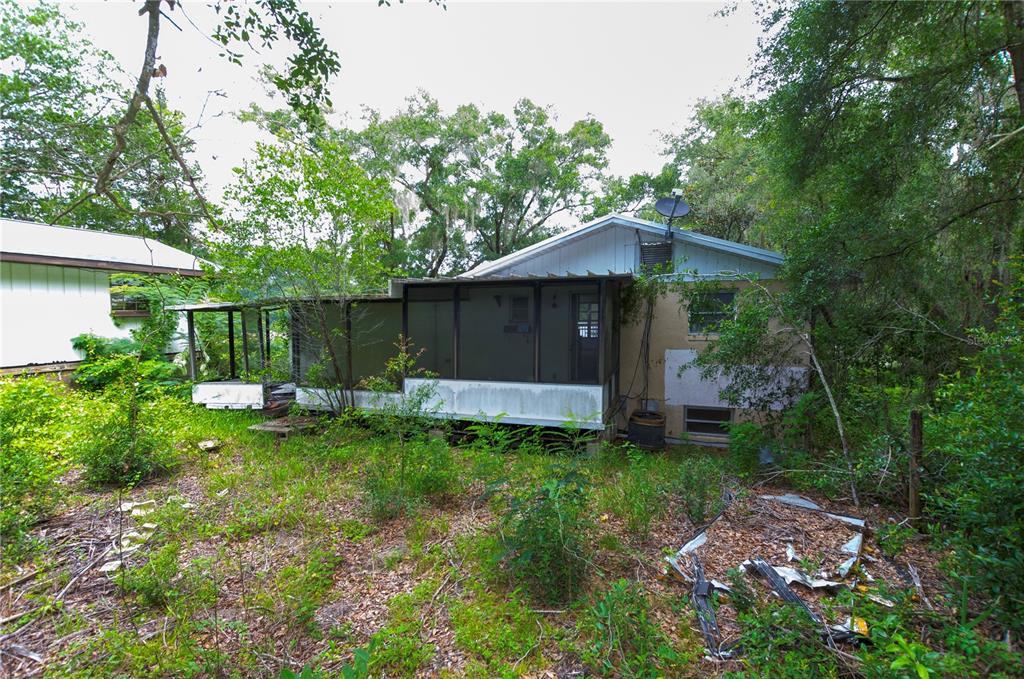 The exterior of a house with a screened-in porch surrounded by overgrown vegetation and trees — 3596 W IVY STREET, DUNNELLON, FL