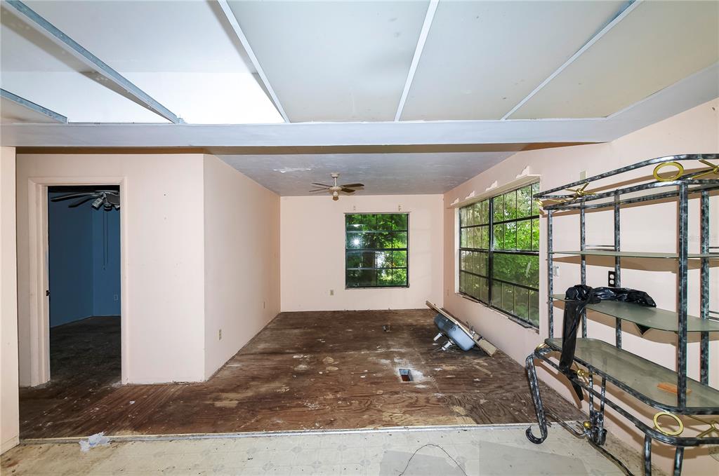 An unfinished room with exposed plywood flooring, a drop ceiling, and a metal shelving unit — 3596 W IVY STREET, DUNNELLON, FL