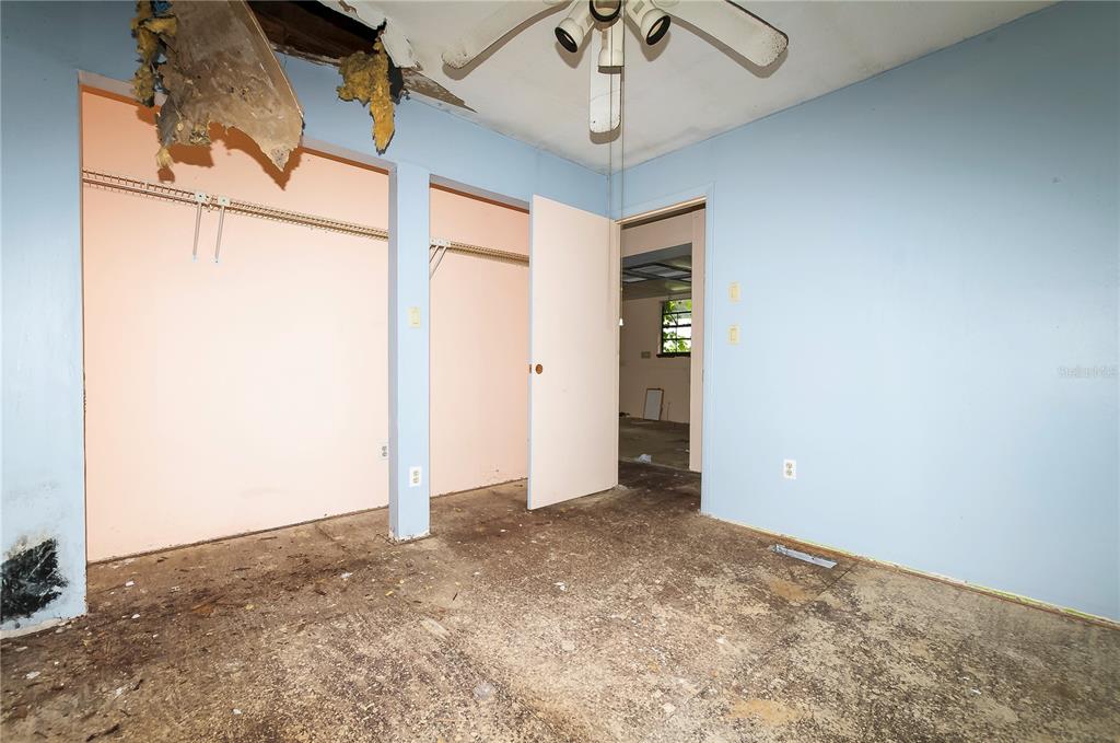 A bedroom with blue walls, a damaged ceiling, and exposed subflooring features two closets — 3596 W IVY STREET, DUNNELLON, FL