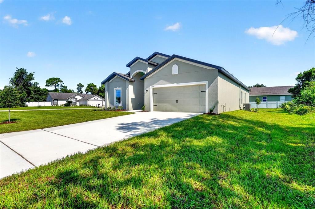 A single-story house with a beige stucco exterior, a two-car garage, and a concrete driveway — 1699 WHIPPLE DRIVE, DELTONA, FL