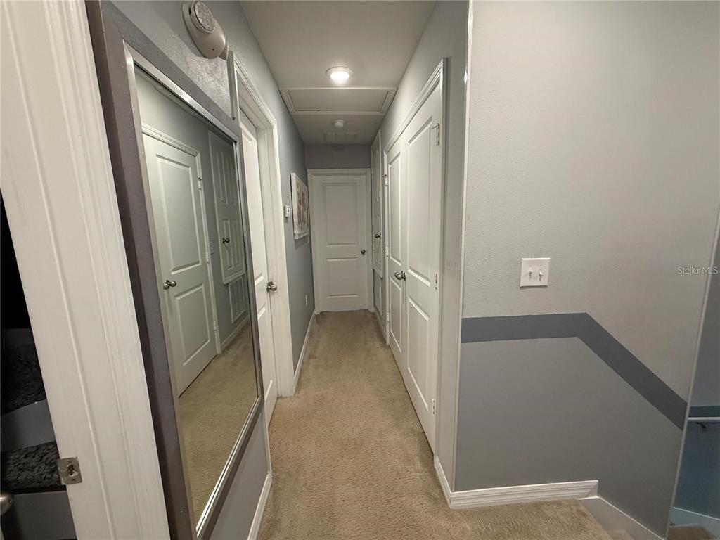 A carpeted hallway features multiple white doors, a large wall mirror, and gray wall paint — 5151 ADELAIDE DRIVE, KISSIMMEE, FL