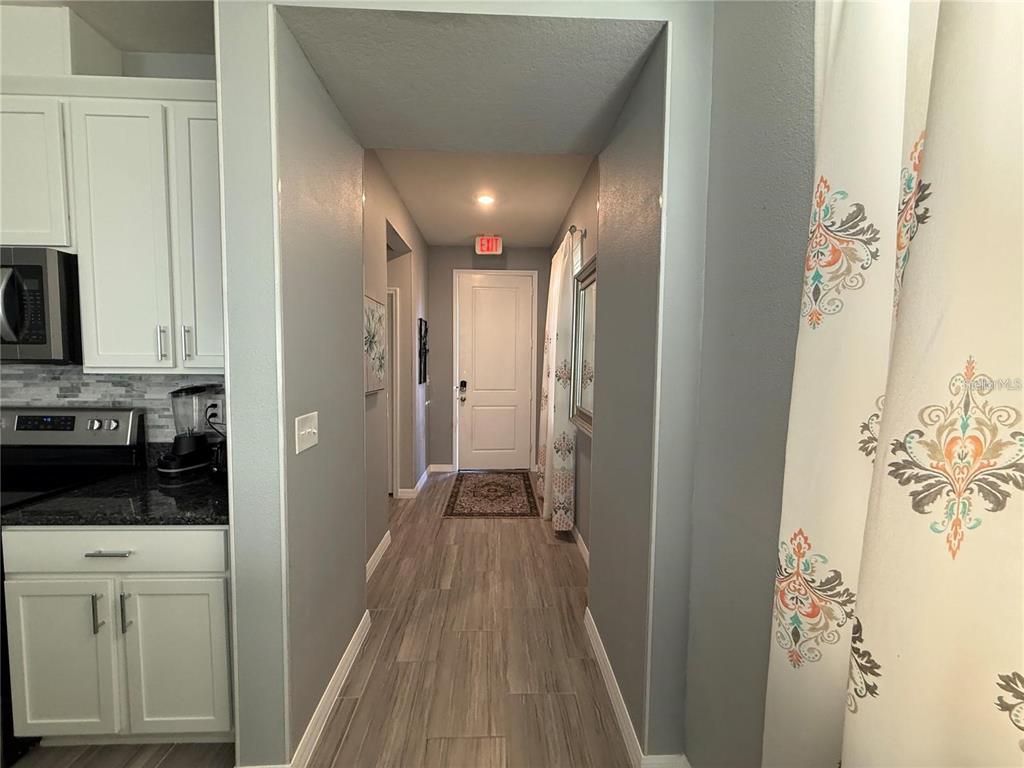 A hallway with wood-look flooring leads to an exterior door with an exit sign above — 5151 ADELAIDE DRIVE, KISSIMMEE, FL