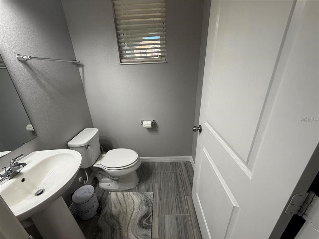 A small bathroom features a pedestal sink, a toilet, and gray wood-look tile flooring — 5151 ADELAIDE DRIVE, KISSIMMEE, FL