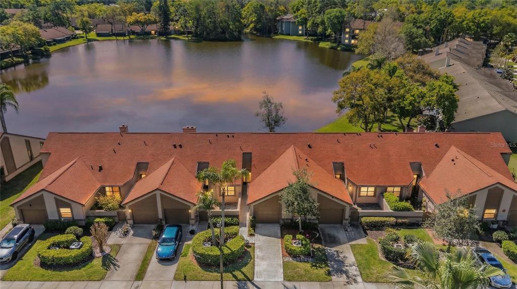 An aerial view shows a row of townhouses with orange roofs facing a lake — 3960 MERMOOR DRIVE, PALM HARBOR, FL