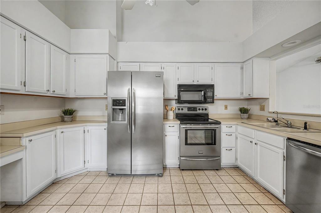 A kitchen with white cabinets, stainless steel appliances, and beige tile flooring — 3960 MERMOOR DRIVE, PALM HARBOR, FL