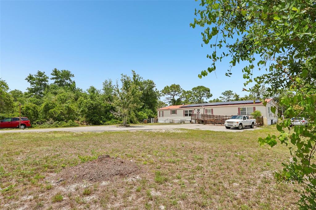 A single-story manufactured home sits on a large, grassy lot with trees and vehicles — 9085 MERCURY DRIVE, ST CLOUD, FL