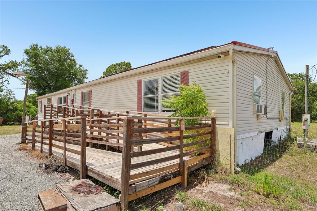 A beige mobile home features a wooden wheelchair ramp leading to the front entrance — 9085 MERCURY DRIVE, ST CLOUD, FL