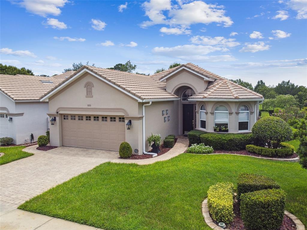 A single-story beige house with a tiled roof, a two-car garage, and landscaped front yard — 521 WESTON PLACE, DEBARY, FL