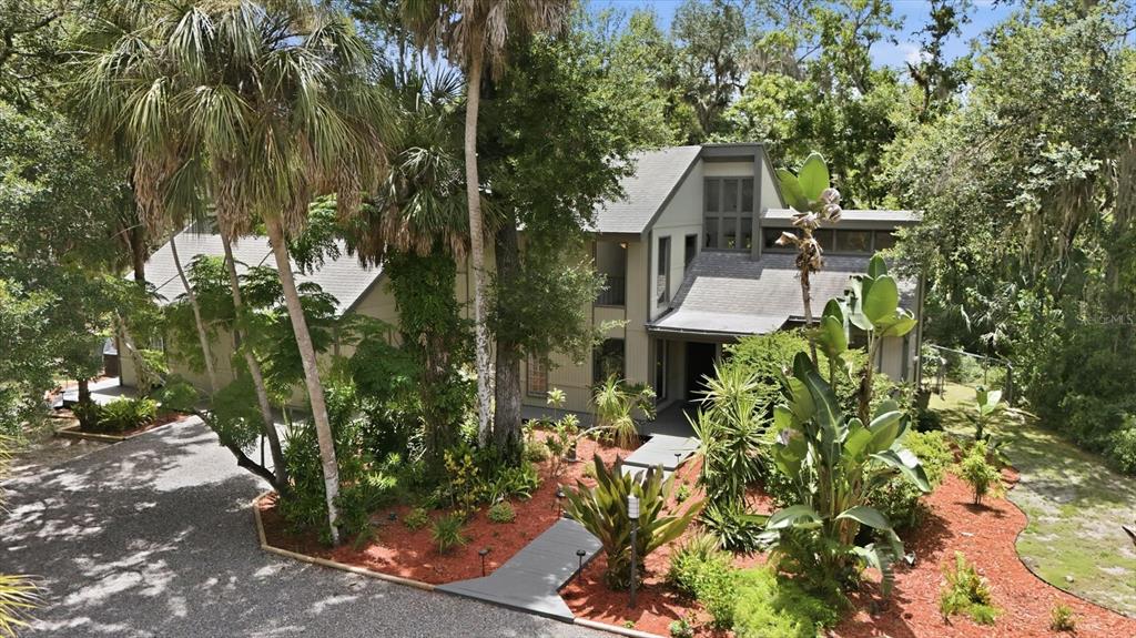 An exterior view of a multi-story house surrounded by lush trees and a gravel driveway — 3805 62ND STREET E, BRADENTON, FL