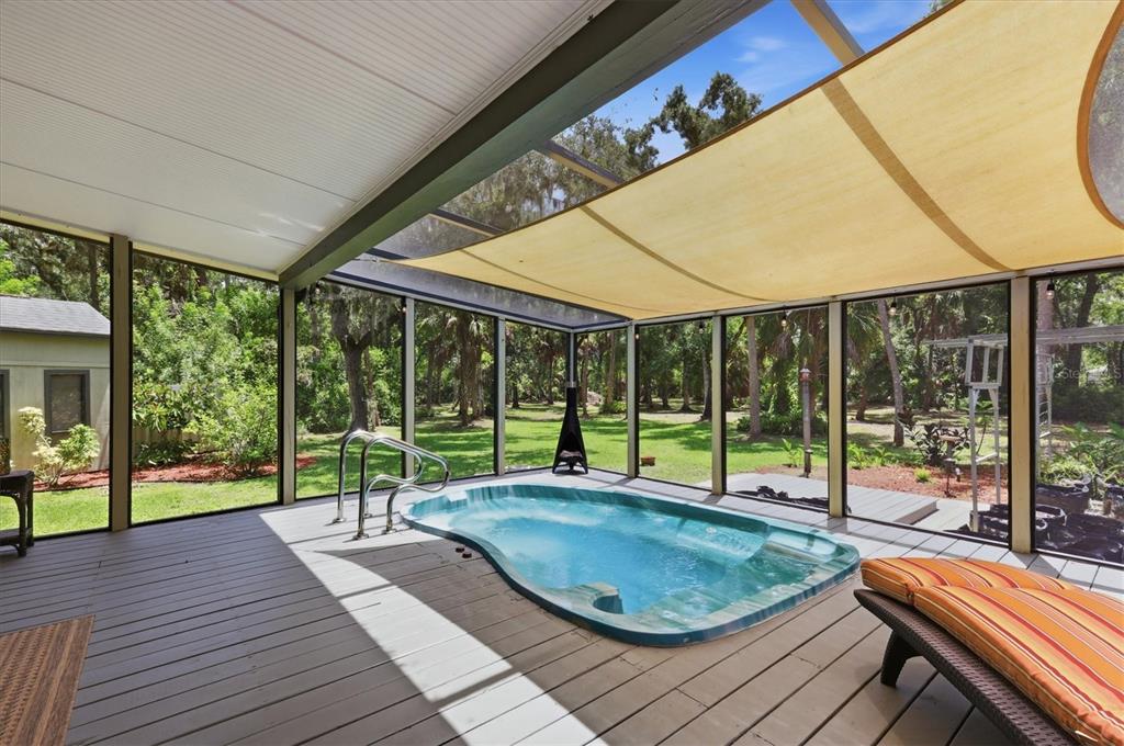 A screened-in deck features a small built-in pool, wooden flooring, and a tan shade sail — 3805 62ND STREET E, BRADENTON, FL