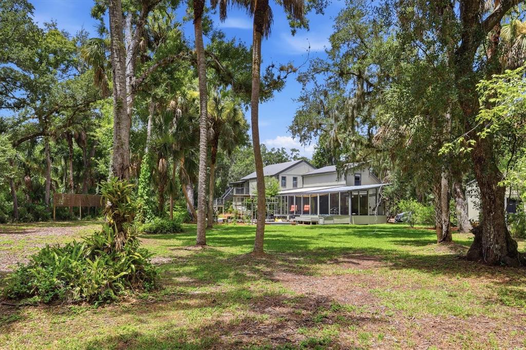 A two-story house with a screened-in porch sits in a wooded yard with palm trees — 3805 62ND STREET E, BRADENTON, FL