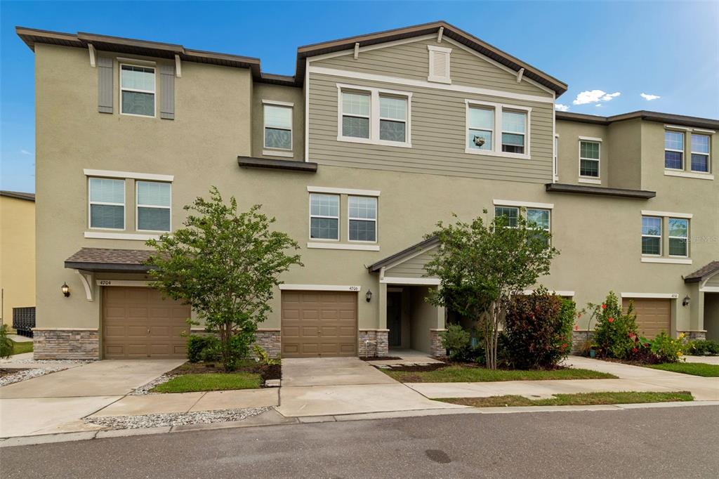 A multi-story townhouse exterior features tan stucco, horizontal siding, and two attached garages — 4706 TUSCAN LOON DRIVE, TAMPA, FL