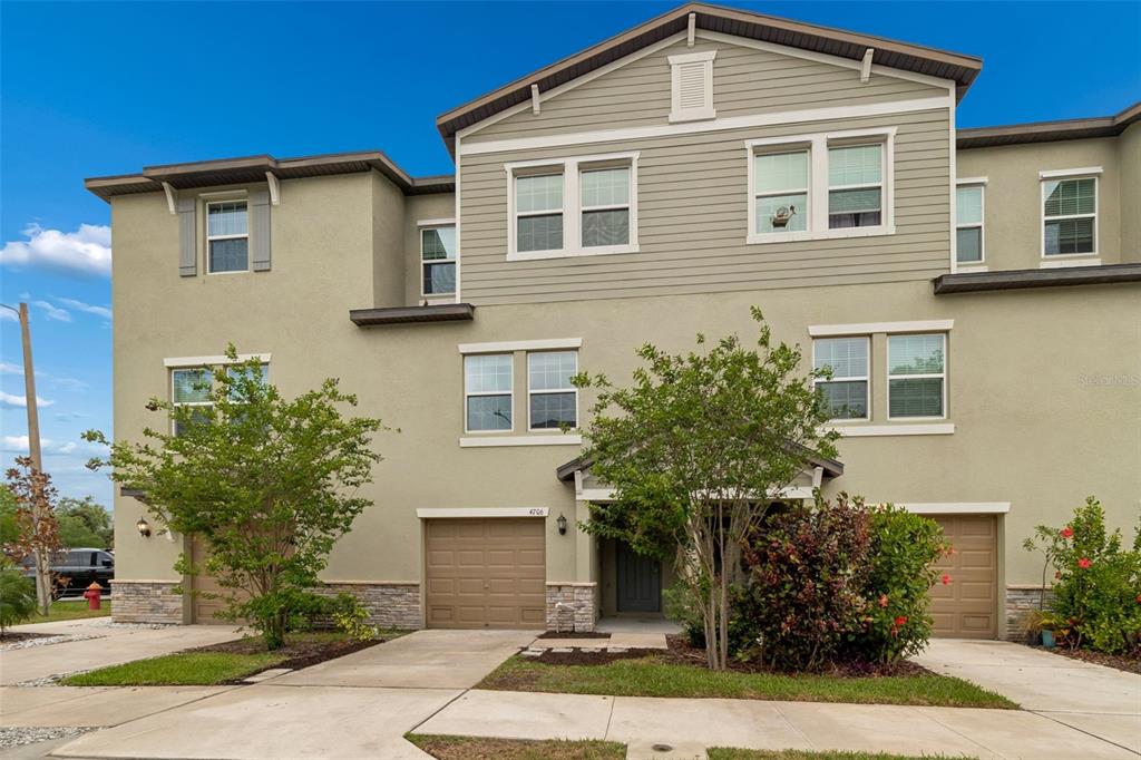 A three-story townhouse with beige stucco and siding, a two-car garage, and a driveway — 4706 TUSCAN LOON DRIVE, TAMPA, FL