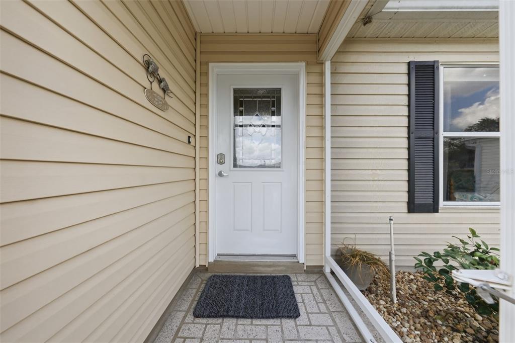 A white front door with a glass insert sits on a porch with stone pavers — 8142 SE 175TH COLUMBIA PLACE, THE VILLAGES, FL