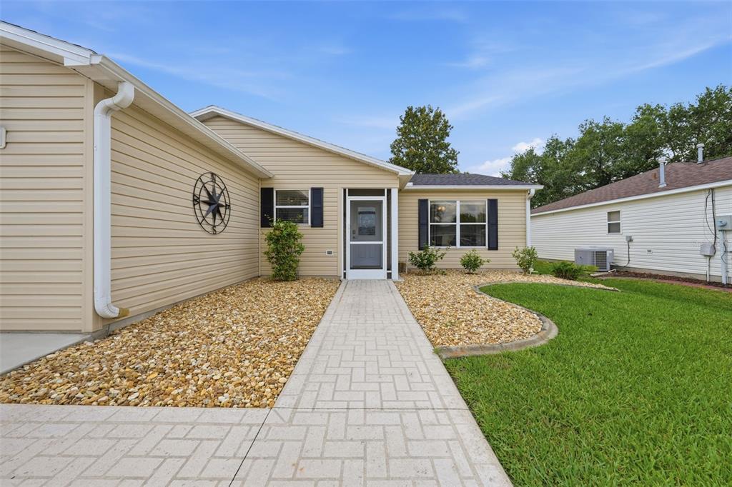 A beige-sided house features a paved walkway leading to a front door with a screen — 8142 SE 175TH COLUMBIA PLACE, THE VILLAGES, FL