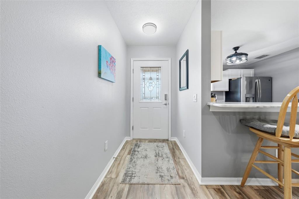 A bright entryway features light gray walls, wood-look flooring, a front door, and a breakfast bar — 8142 SE 175TH COLUMBIA PLACE, THE VILLAGES, FL