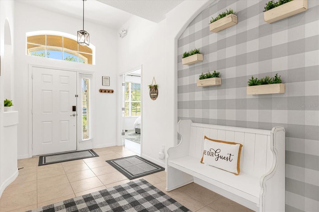 A bright entryway features a white bench, buffalo check wallpaper, and wall-mounted wooden planters — 308 YELLOW SNAPDRAGON DRIVE, DAVENPORT, FL