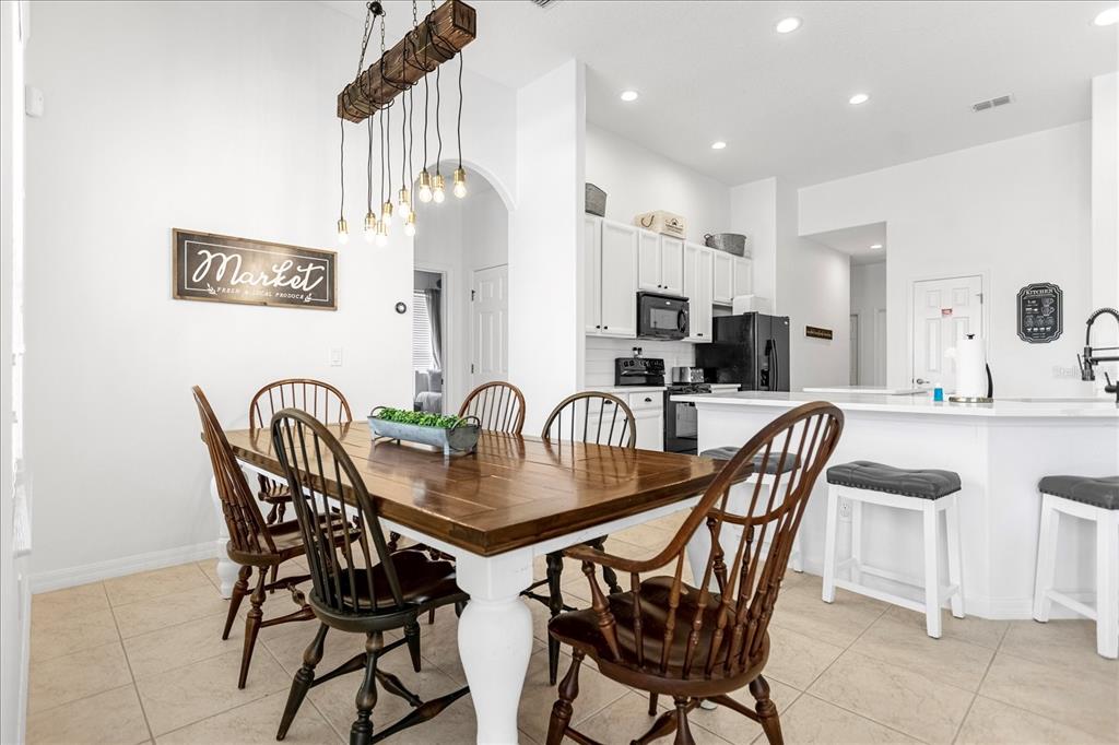 A dining area with a wooden table and chairs sits adjacent to a white kitchen — 308 YELLOW SNAPDRAGON DRIVE, DAVENPORT, FL
