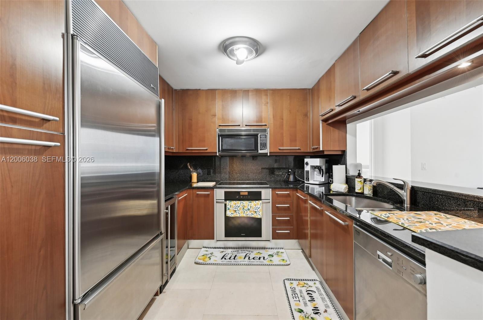 A galley kitchen features wood cabinets, stainless steel appliances, and black granite countertops — 901 Brickell Key Blvd # 1009, Miami FL 33131, MIAMI, FL