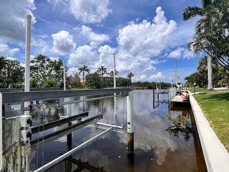 A boat lift stands over a canal with palm trees and houses in the background — 5530 ALMAR DRIVE, PUNTA GORDA, FL
